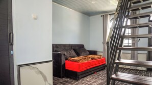 Ein Zimmer mit einer schwarzen Couch, einer roten Aufbewahrungsbox, einer Holztreppe und einem Fliesenboden.