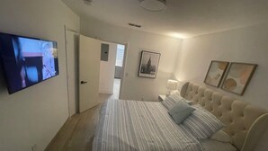 A bedroom with a bed, a TV, a door, a framed picture, and a nightstand. - luxury cozy apartment for couples only (Hallandale Beach)