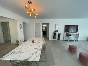 Een moderne woonkamer met een marmeren eettafel, een kroonluchter, een televisie en een potplant.