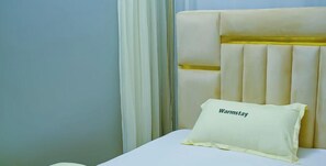 En säng med en sänggavel, en kudde med etiketten ”Warmstay” och ett vitt sängöverkast.