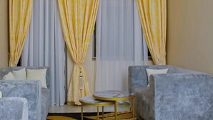 Une pièce avec deux canapés gris, une petite table ronde et des rideaux jaunes.