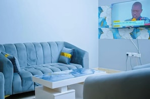 Ett modernt vardagsrum med en grå soffa, ett vitt soffbord och en platt-TV som är monterad på väggen.
