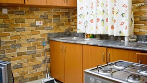 Une cuisine avec un mur en briques, des placards en bois, une cuisinière à gaz et un rideau orné de motifs de fruits.