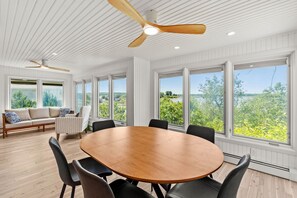 Una habitación amplia con una gran mesa de madera, asientos cómodos y ventanas grandes que ofrecen vistas a la vegetación.