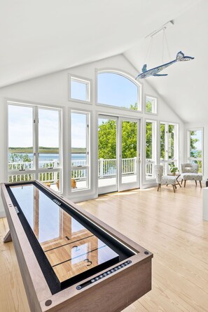 A room with a pool table, large windows, and a view of a lake. - Plumb Island Sound Waterfront Sunset Getaway (Ipswich)