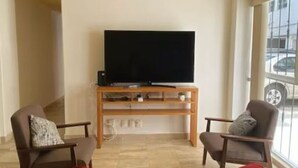 A living room with a flat-screen TV on a wooden stand, two armchairs, a red sofa, and a large window with a view of the street. - Del Valle Norte, just steps from the WTC, on the ground floor. (Ciudad de México)