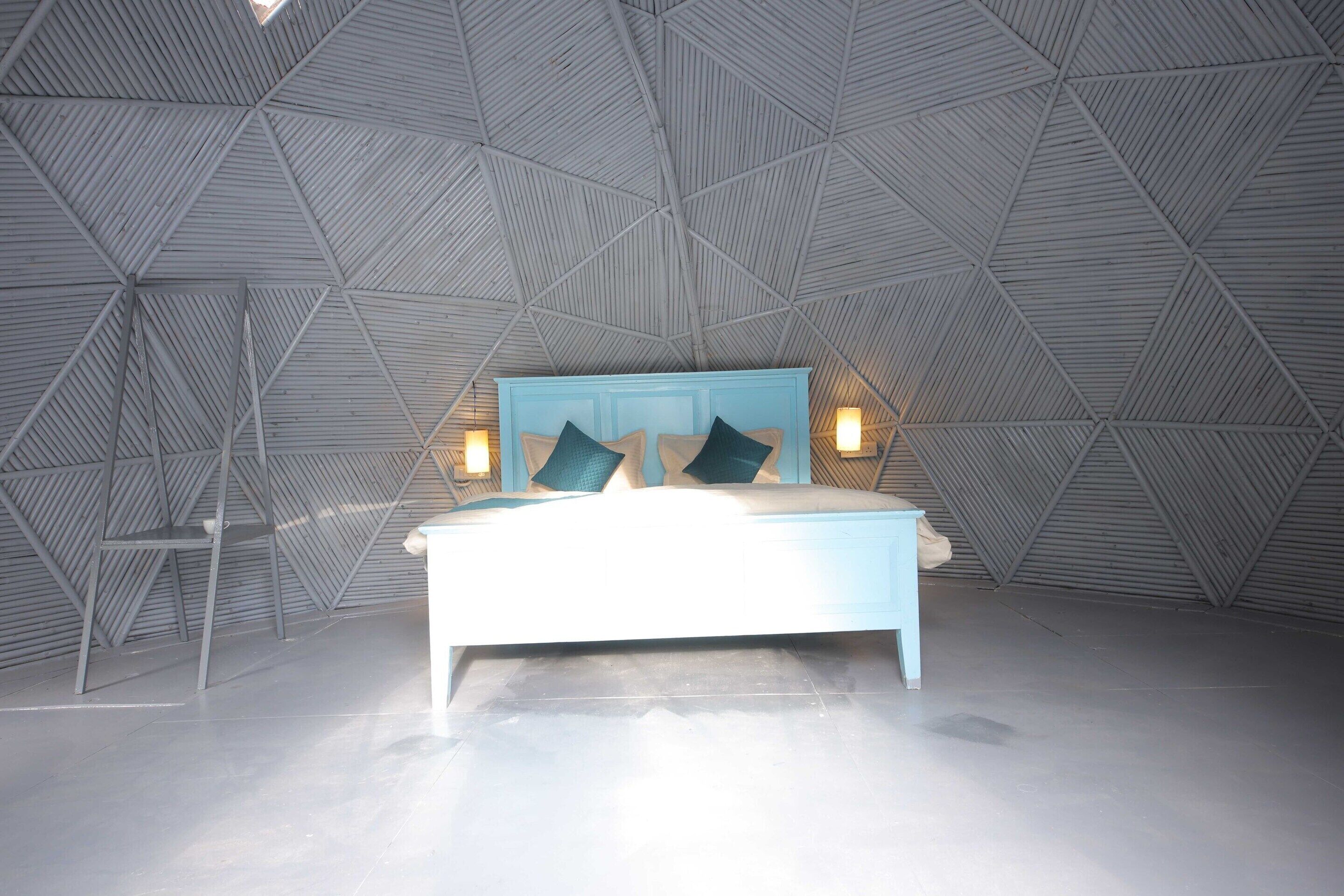 Quarto moderno com teto geométrico, cama com cabeceira azul e duas luminárias de apoio.