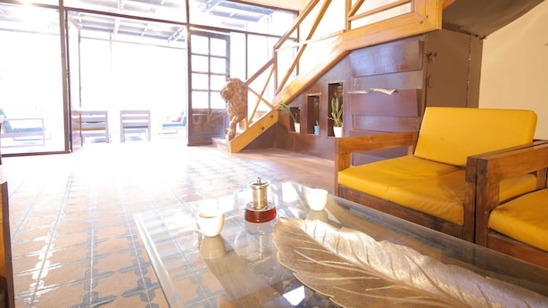 Een kamer met een glazen tafel, een houten trap en gele fauteuils.