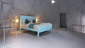 Een kamer met een plafond met een geometrisch patroon, een bed met een lichtblauwe lijst, en een stoel.