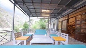 Een overdekt terras met wit en blauw meubilair, uitzicht op een bergachtig landschap en een houten deur met een standbeeld van een leeuw.