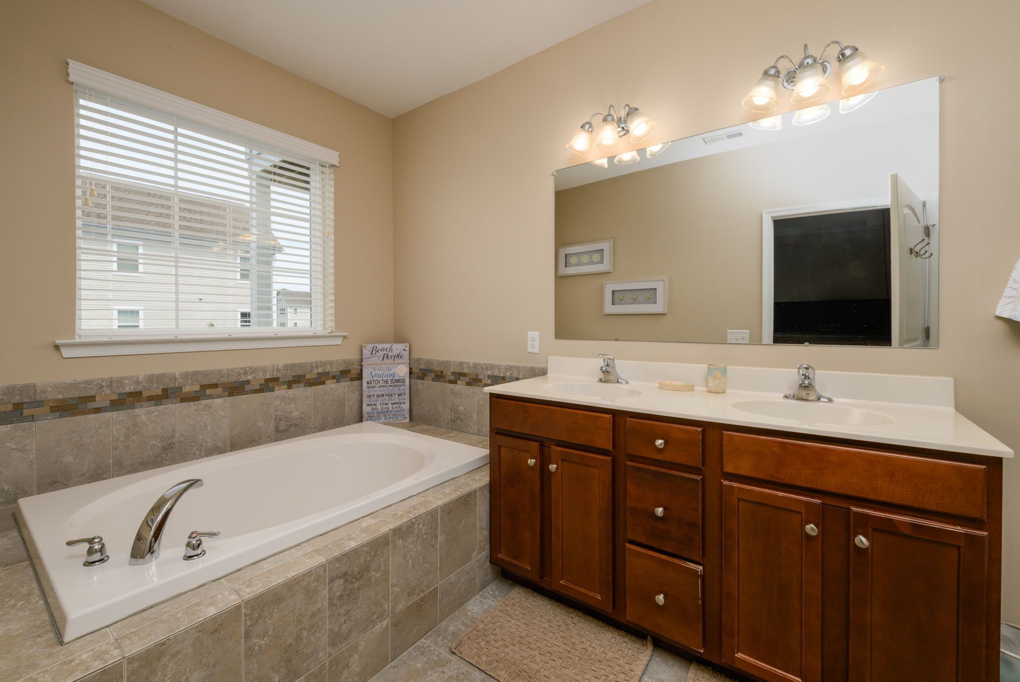A bathroom with a bathtub, vanity with a mirror, and a window with blinds.