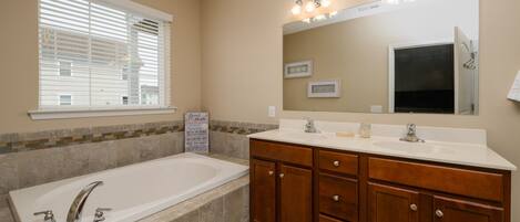 A bathroom with a bathtub, vanity with a mirror, and a window with blinds.