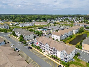 An aerial view of a residential area with apartment buildings, a parking lot, and a river. - Beautiful Rehoboth Beach Condo Pools Tennis Parking (Rehoboth Beach)