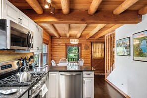 Eine moderne Küche mit Edelstahlgeräten, Holzbalkendecke und einer Essecke mit weißen Stühlen.