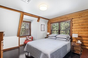 Un dormitorio con cama, mesita de noche, silla y ventana con vista a árboles.