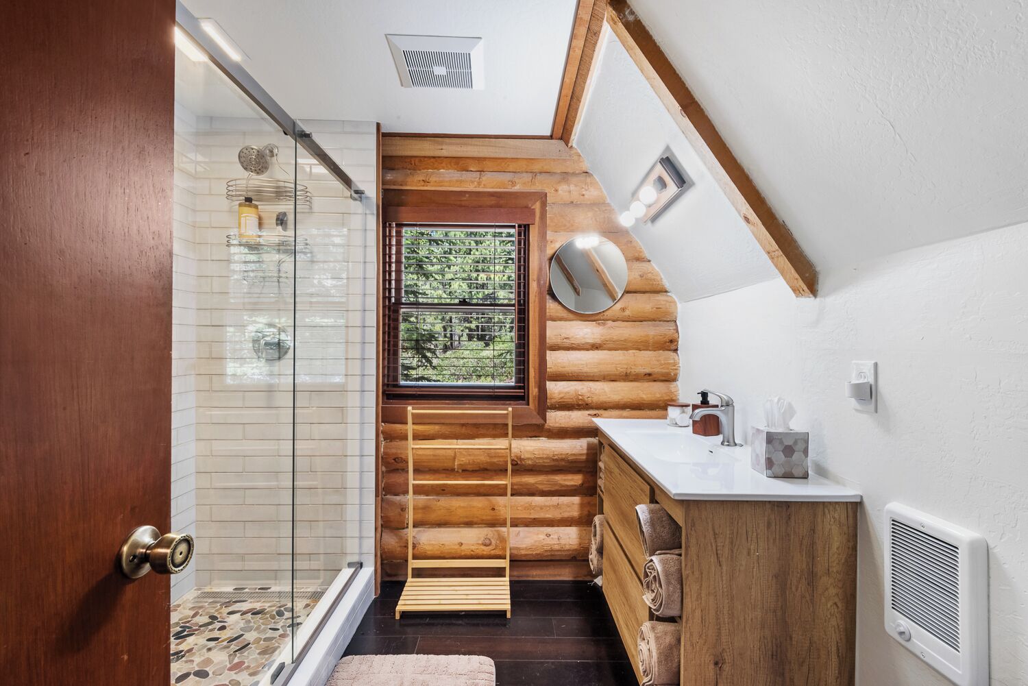 A log cabin bathroom with a shower, a window with a view, a sink, and a mirror.