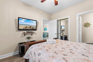 Un dormitorio con cama, televisión, escritorio y puerta que da a otra habitación.