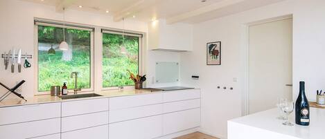 Una cocina moderna con armarios blancos, un ventanal grande y una zona de comedor con una botella de vino y copas.