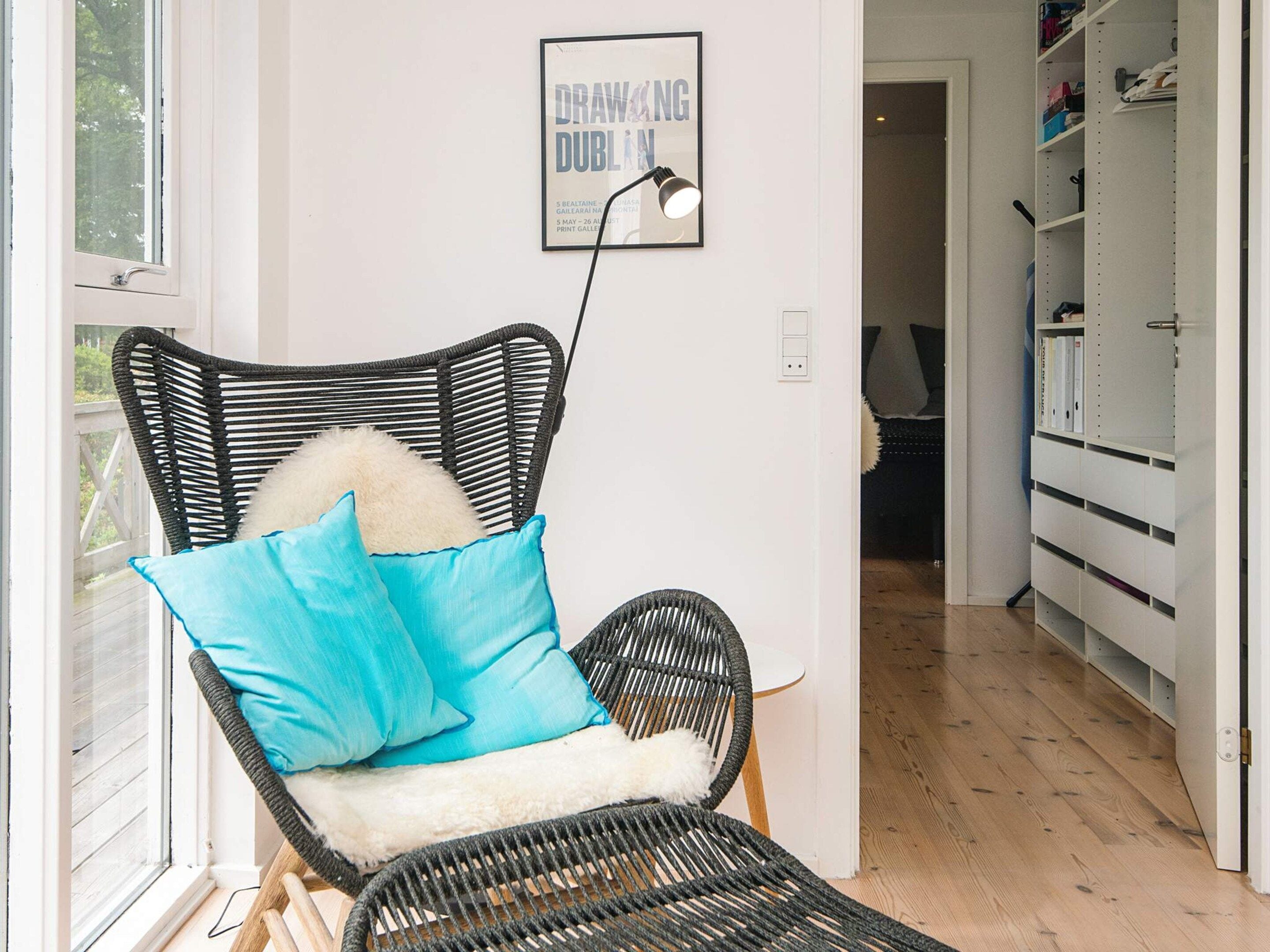 A room with a wicker chair, a framed poster on the wall, and a white storage unit.