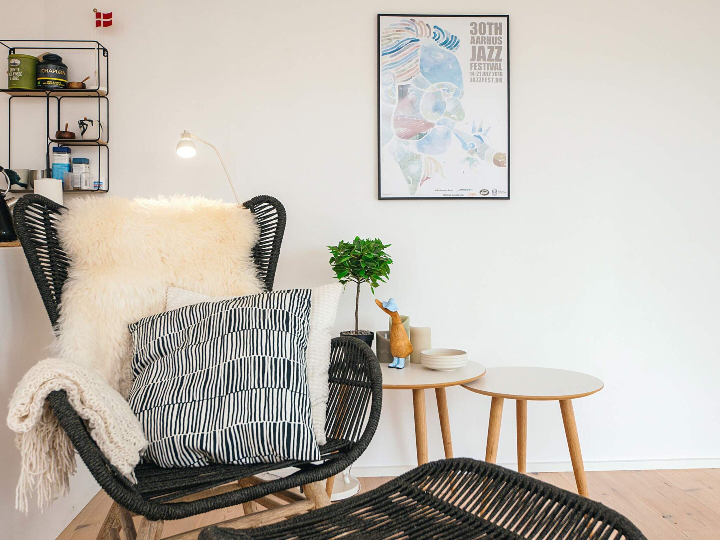 A modern living room with a black wicker chair, a round wooden table, and a framed poster on the wall.