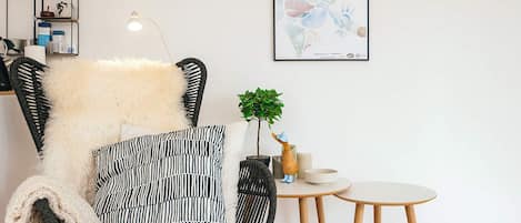 A modern living room with a black wicker chair, a round wooden table, and a framed poster on the wall.