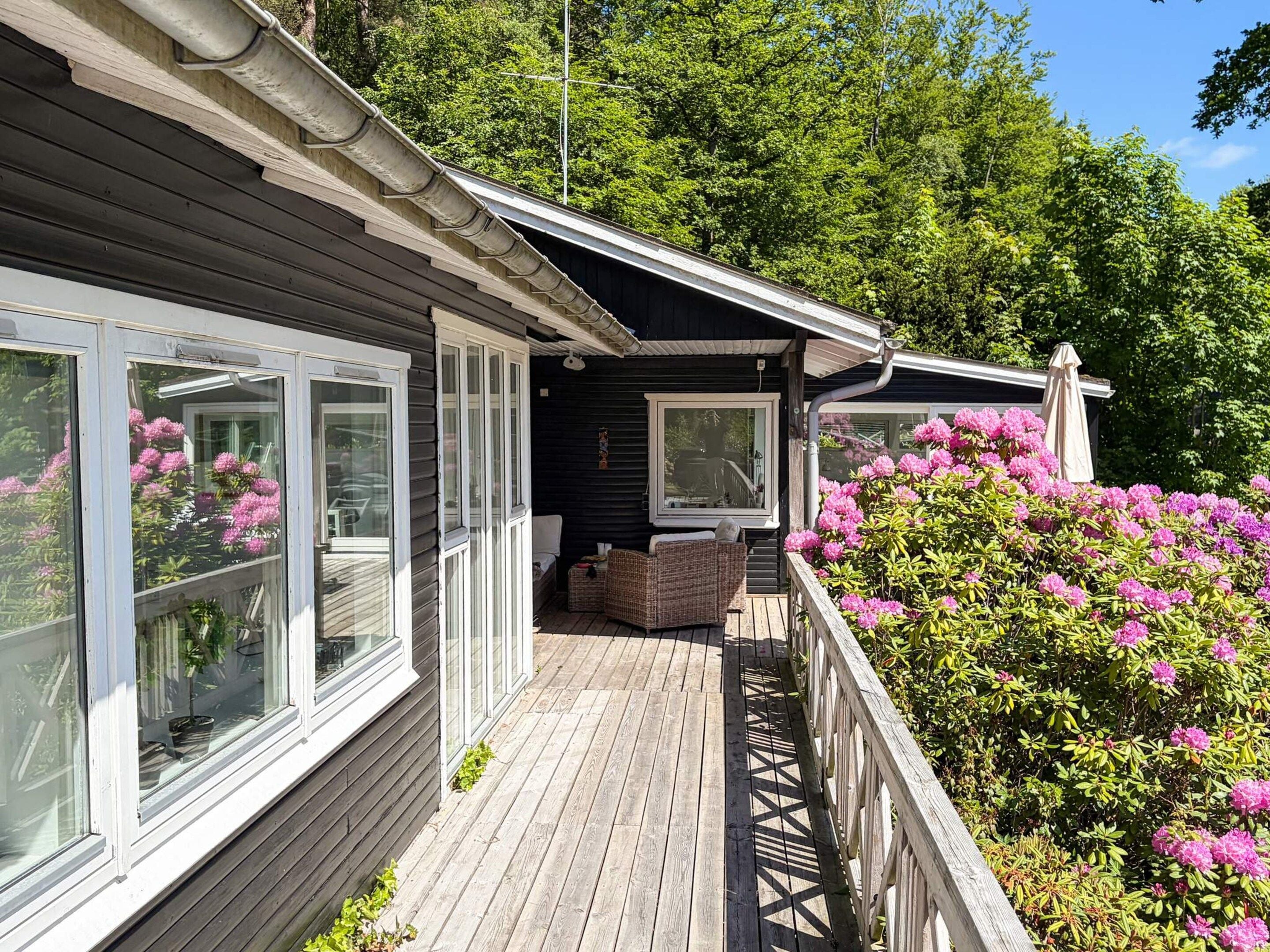 A wooden deck with a railing, a covered seating area, and a view of a garden with pink flowers.