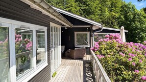 A wooden deck with a railing, a covered seating area, and a view of a garden with pink flowers. - 4 Star Holiday Home in Silkeborg (Silkeborg)