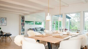 A modern dining area with a wooden table, white chairs, and large windows offering a view of greenery. - 4 Star Holiday Home in Silkeborg (Silkeborg)