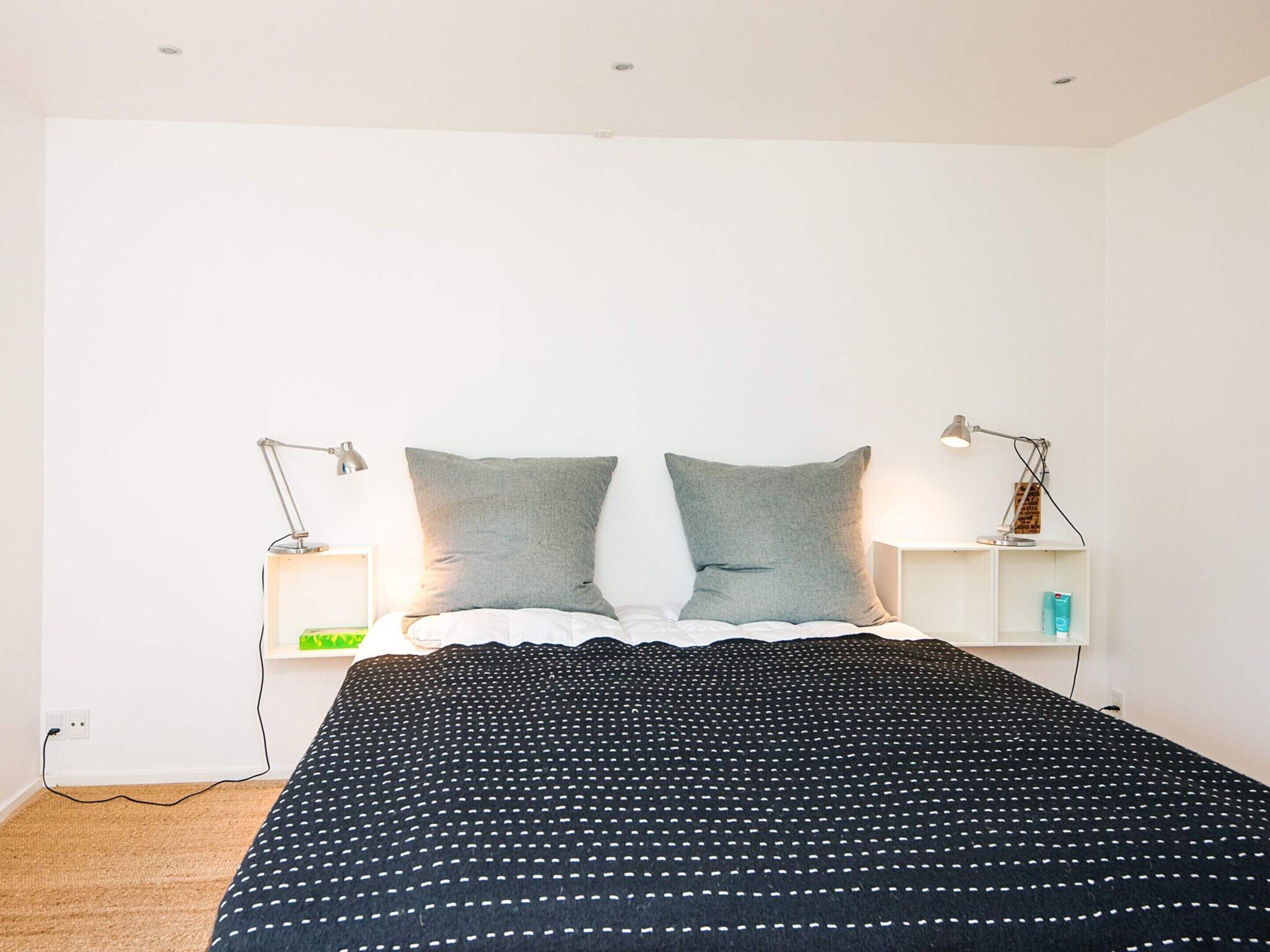 Une chambre à coucher avec un lit, deux oreillers, deux tables de chevet avec des lampes et une petite table de nuit avec une lampe.