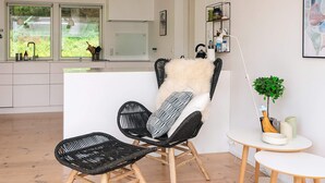 A modern living room with a black wicker chair, a small white table, and a view of the kitchen and garden through large windows. - 4 Star Holiday Home in Silkeborg (Silkeborg)
