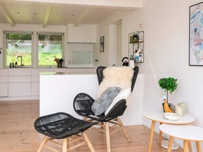 A modern living room with a black wicker chair, a small white table, and a view of the kitchen and garden through large windows. - 4 Star Holiday Home in Silkeborg (Silkeborg)