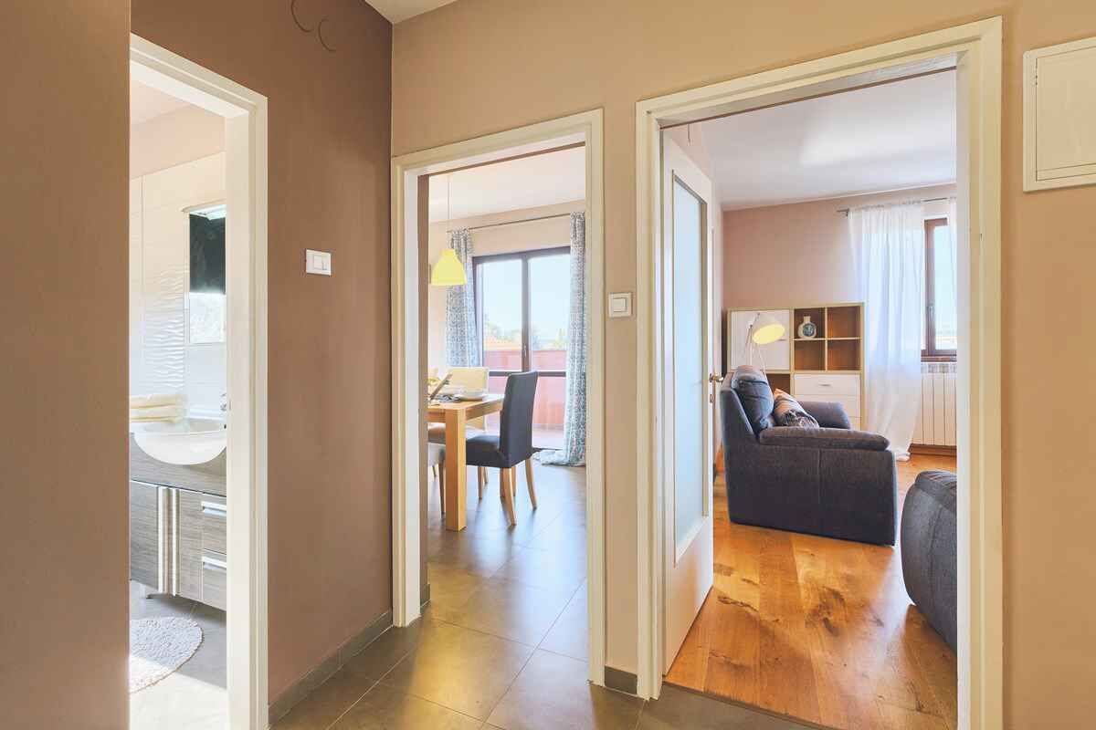 A hallway leading to a dining area with a table and chairs, a sofa, and a kitchen area with a counter and cabinets.