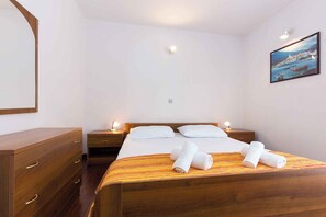 A hotel room with a wooden bed, two bedside tables with lamps, a wooden dresser, and a framed picture on the wall. - Holiday apartment near the sea for 6 people (Punat)