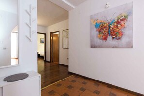 A hallway with a wooden floor, a white wall with a colorful butterfly painting, and a door leading to a room. - Holiday apartment near the sea for 6 people (Punat)