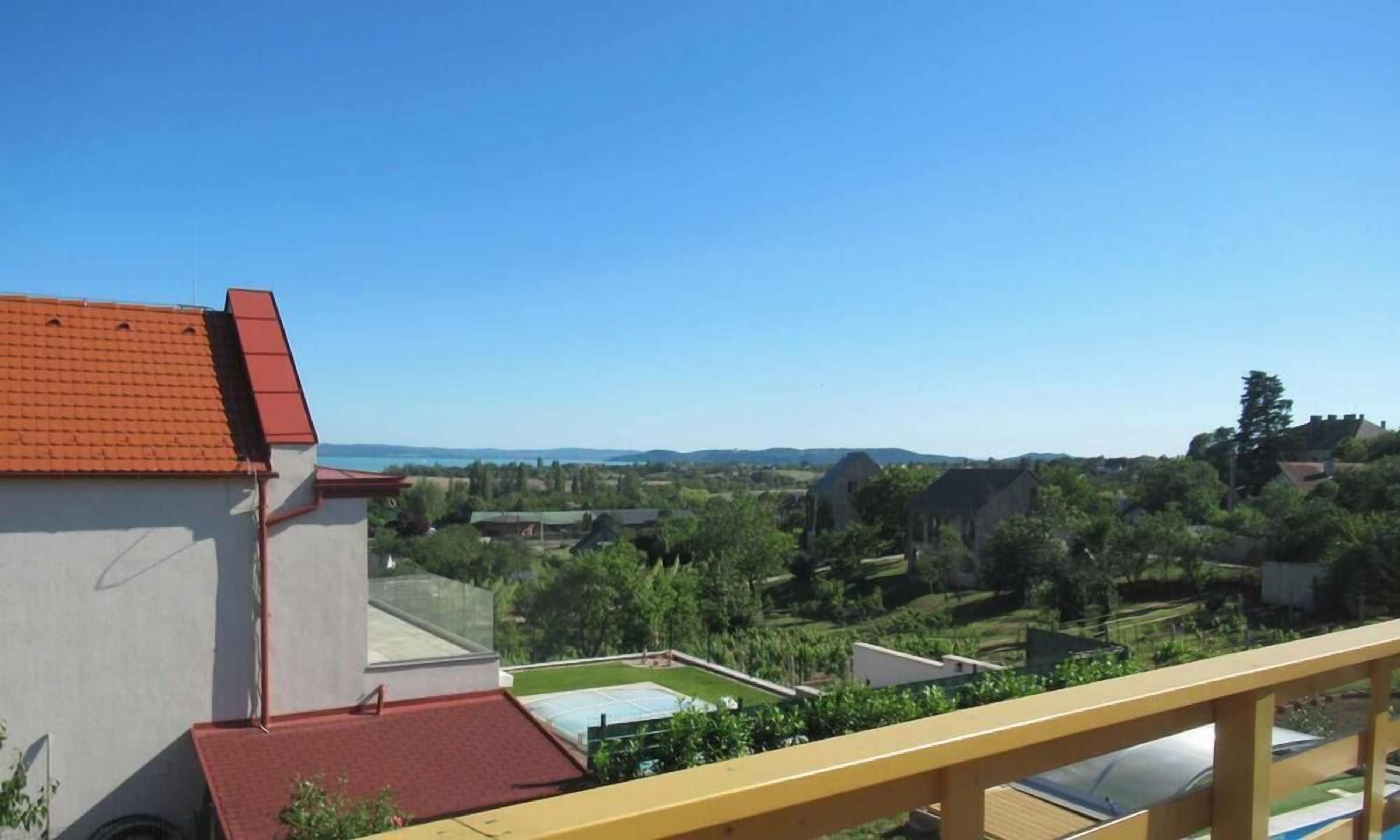 A residential building with a red roof, a balcony, and a view of a green landscape with houses and trees.
