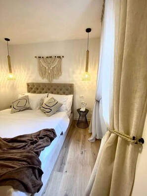 Ein Schlafzimmer mit einem Bett, zwei Hängelampen, einem Wandbehang aus Makramee, einem Nachttisch und einem Vorhang.
