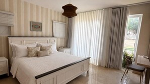 Un dormitorio con una cama grande, una mesita de noche, una lámpara colgante y un ventanal con cortinas.