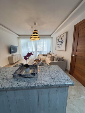 A modern living room with a central island, a sofa set, a television, and a painting on the wall. - Relaxing Beach Apartment with pool, jacuzzi, beach in RivieraGolf Playa Dorada (Playa dorada)