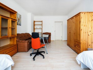 Ein Zimmer mit einem Holzschrank, einem braunen Ledersofa, einem roten Bürostuhl, einem weißen Bett und einem Holztisch mit einem Computer.