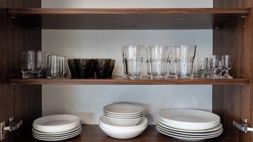 A wooden cabinet with shelves holding clear glasses, black bowls, and white plates.