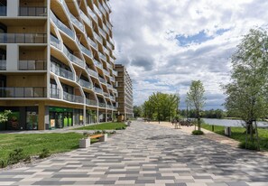 Ein modernes, mehrgeschossiges Gebäude mit Balkonen, einem gepflasterten Weg und Blick auf einen See.