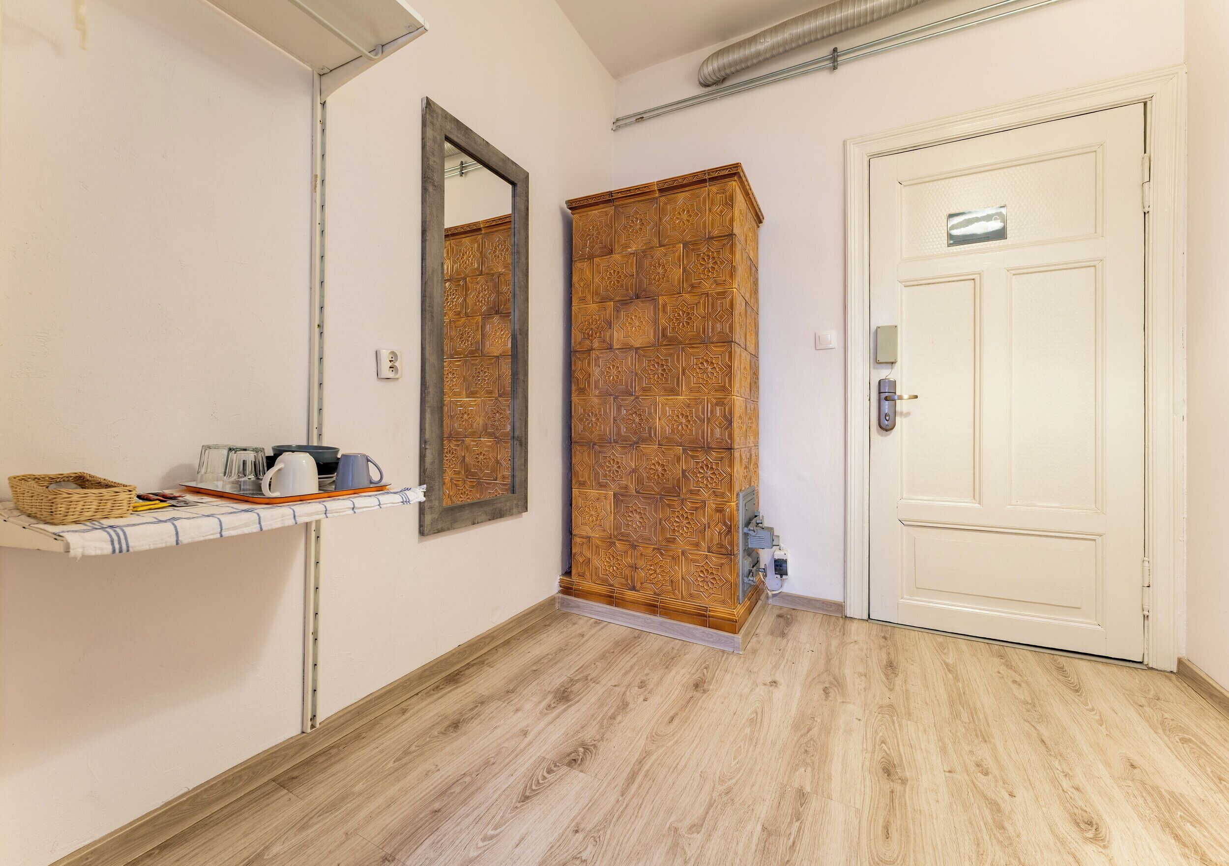 Un couloir avec une armoire en bois, un miroir, une porte et une étagère sur laquelle sont posés divers objets.