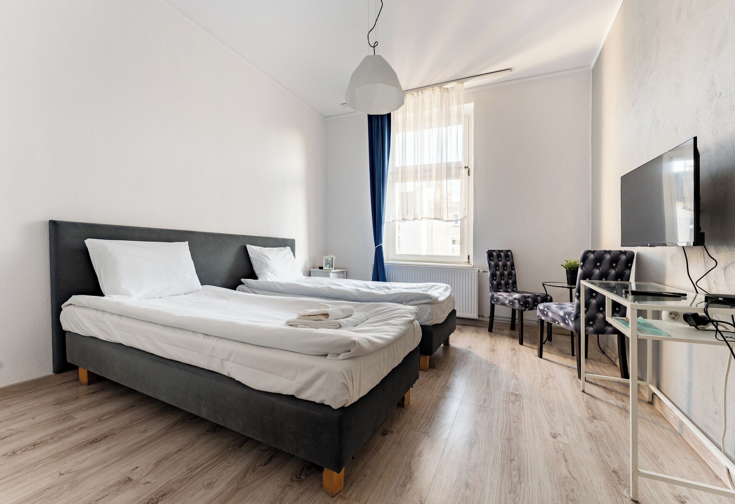 A modern hotel room with two beds, a desk, a chair, a TV, and a window with curtains.