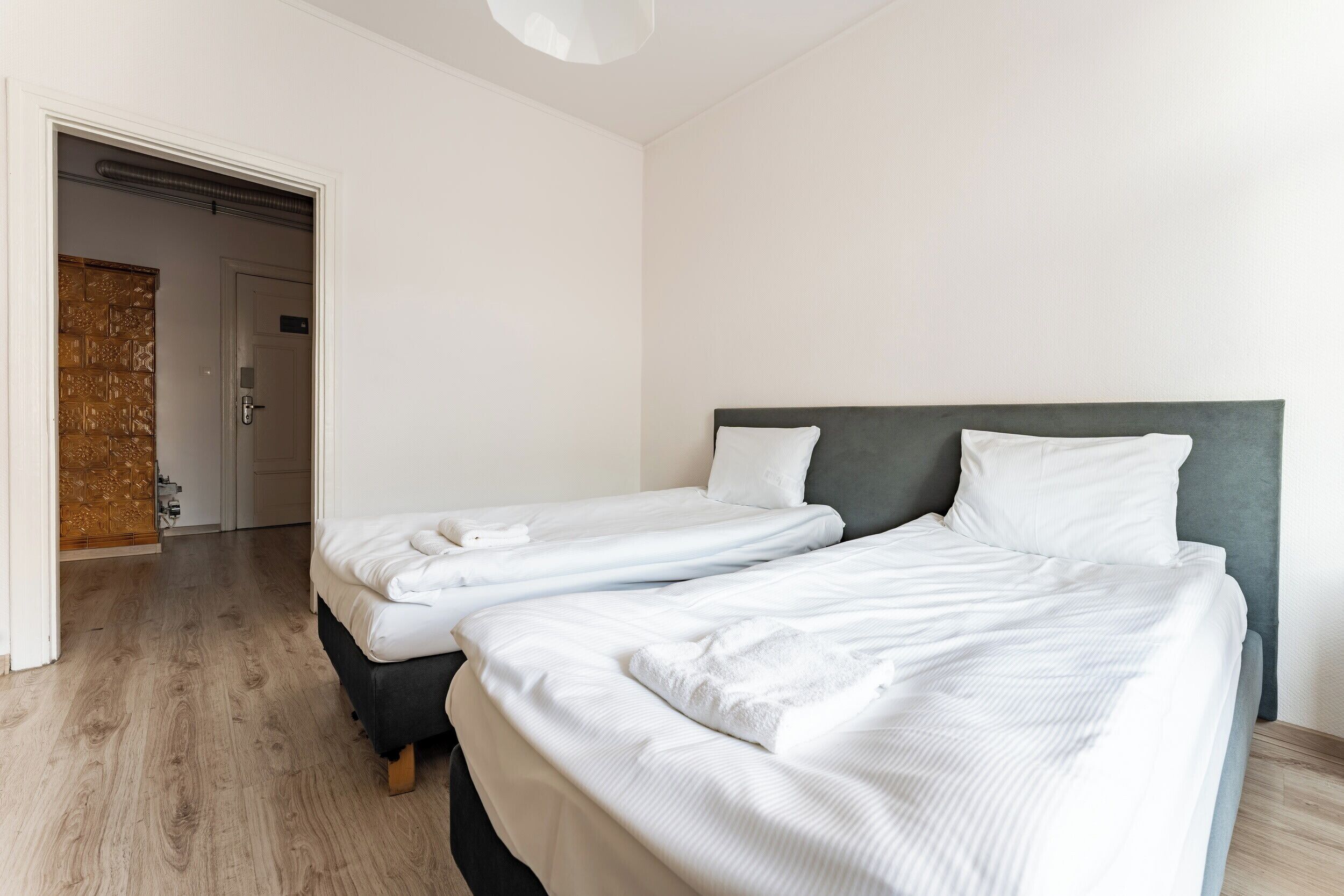 A hotel room with two beds, a wooden floor, and a door leading to a bathroom.