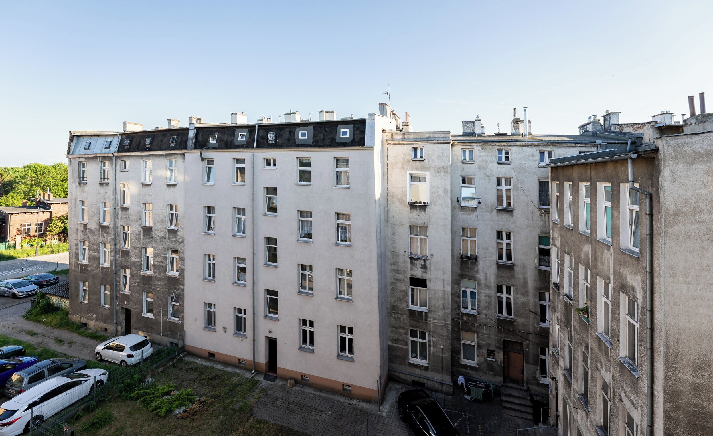 Ein mehrgeschossiges Gebäude mit einer flachen Fassade, vielen Fenstern und einem Parkplatz mit Autos.