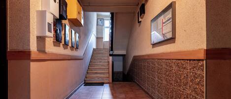 A hallway with a tiled floor, a staircase, and a wall-mounted bulletin board.