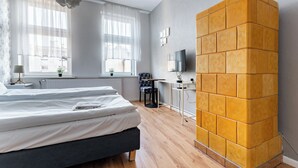 A bedroom with a bed, a desk, a chair, a TV, and a unique yellow brick wall. - Gdańsk Hostel Octopus Studio #3 (Gdańsk)
