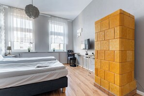 A bedroom with a bed, a desk, a chair, a TV, and a unique yellow brick wall. - Gdańsk Hostel Octopus Studio #3 (Gdańsk)