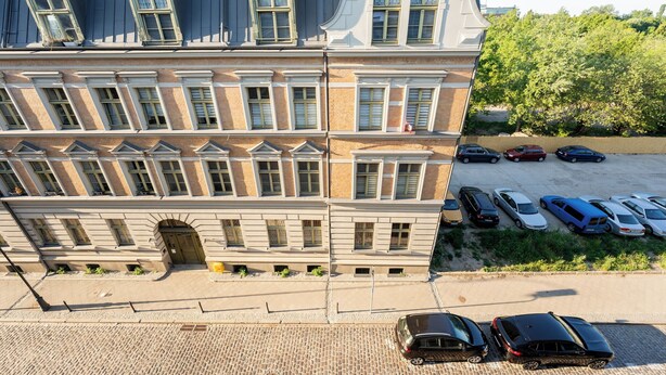 En byggnad med flera våningar, framför vilken en rad parkerade bilar står.