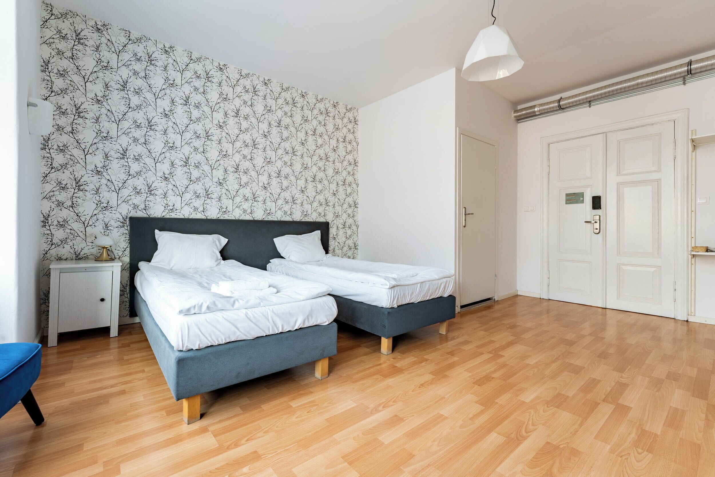 Ein Schlafzimmer mit zwei Betten, einem Nachttisch, einer Lampe und strukturiertem Wandpapier.
